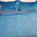 Blue textured bedding set with matching pillows on a bed.