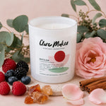 A white glass candle jar labeled Clare Makes Matilda, styled with pink roses, raspberries, blueberries, cinnamon sticks, and rose petals on a soft pink surface.