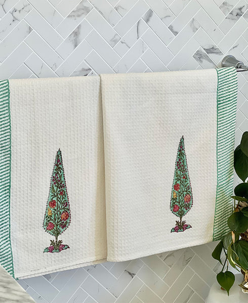 Two towels with tree designs hanging on a rack against a marble wall.