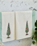 Two towels with tree designs hanging on a rack against a marble wall.