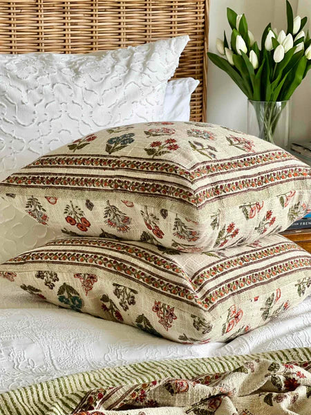 Decorative pillows with floral patterns on a bed with white bedding and a vase of tulips.
