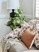 Decorative pillows and blanket on a sofa with a lamp and plant in the background.