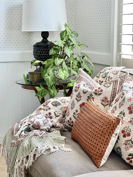 Decorative pillows and blanket on a sofa with a lamp and plant in the background.
