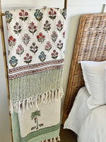 Decorative blanket with floral patterns draped over a wooden ladder against a bed with wicker headboard.