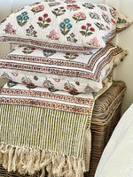 Stack of patterned fabric items including a blanket and pillows on a woven basket.