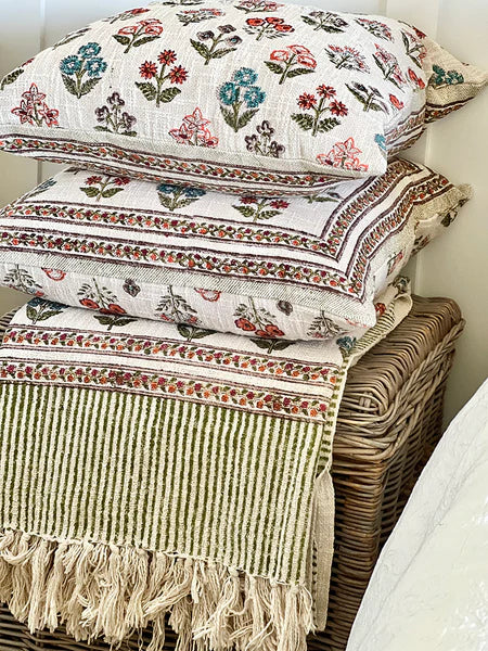 Stack of patterned fabric items including a blanket and pillows on a woven basket.