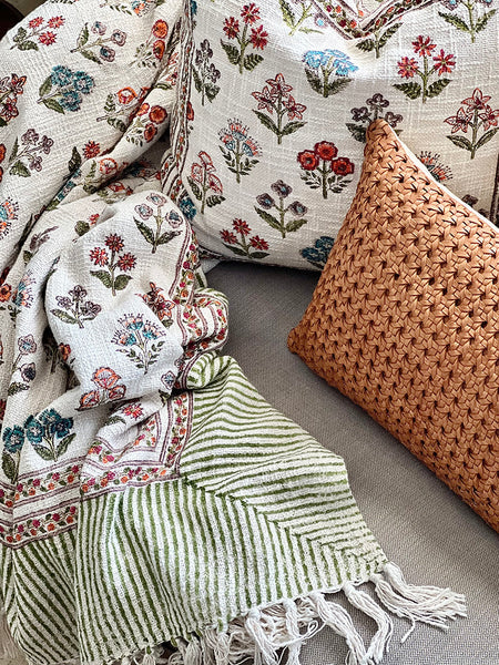 Floral-patterned pillows and a green striped blanket on a sofa.
