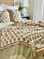 Decorative floral quilt on a bed with pillows and a lamp in the background