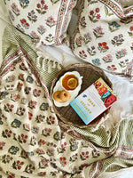 Floral-patterned fabric with a woven basket containing tea and cookies.