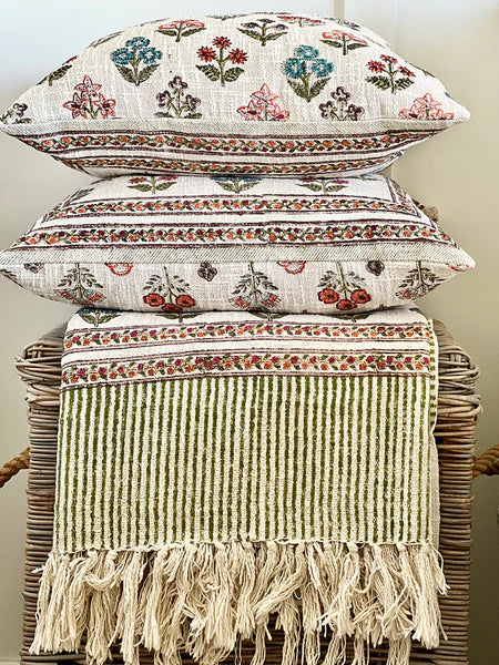 Stack of decorative pillows with floral patterns on a wicker chair.