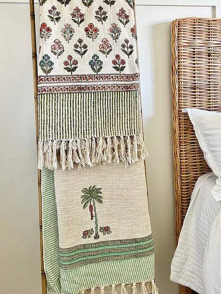 Decorative throw blanket with floral and palm tree patterns hanging on a wall next to a bed with a wicker headboard.