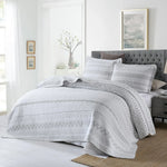 Gray quilt set on a bed in a bedroom with white walls and framed art.