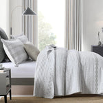 Bedroom with a bed covered in a patterned gray and white comforter, pillows, and nightstands.