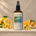 A bottle of Of The Sea Tarot Collection Limoncello uplifting room spray, styled on a marble surface with lemons, citrus slices, and a crystal cluster against a textured stone background.