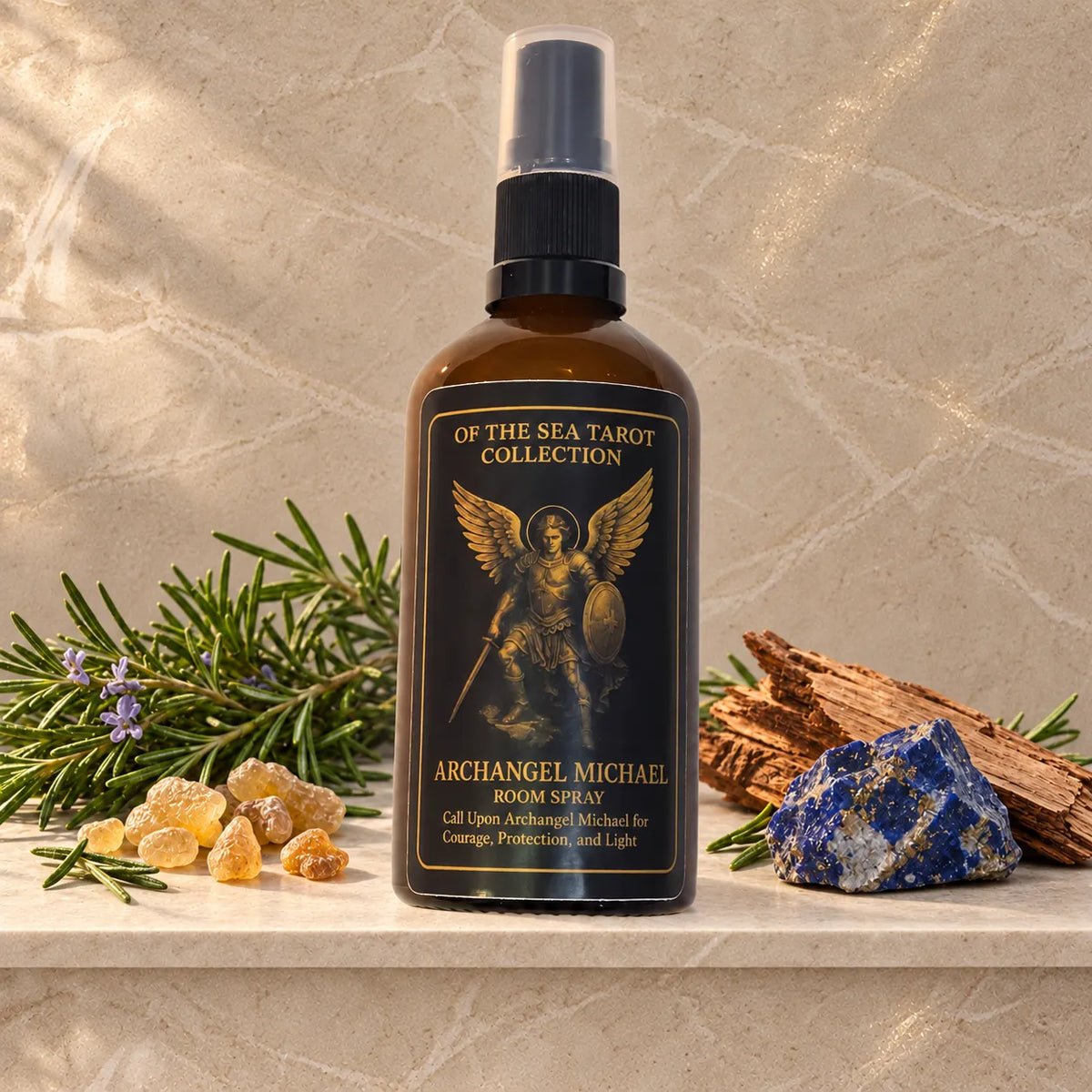A bottle of Archangel Michael Room Spray from the 'Of the Sea Tarot Collection' displayed on a marble shelf with natural props including a crystal, rosemary, and wood shavings against a textured stone background.
