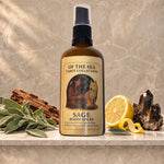 A bottle of Sage Room Spray from The of the Sea Tarot Collection sits on a marble shelf styled with sage leaves, a lemon half, and crystals against a textured beige background.