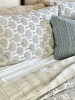 Patterned bedding with a tree design on a bed with a gray textured pillow.