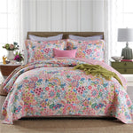 Floral bedding set on a bed in a bedroom with a lamp and table.