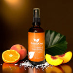 Bottle of Calm & Cozy Orange & Peach Blossom product with fruits and salt on a reflective surface.