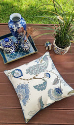 Decorative pillow with floral pattern on a wooden surface with a tray of decorative items.