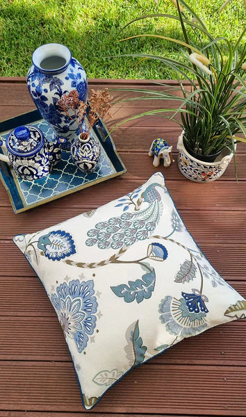 Decorative pillow with floral pattern on a wooden surface with a tray of decorative items.