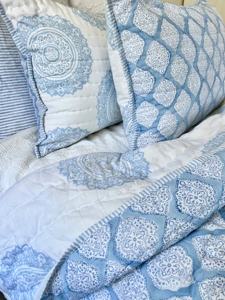 Blue and white patterned quilt with matching pillows on a bed.