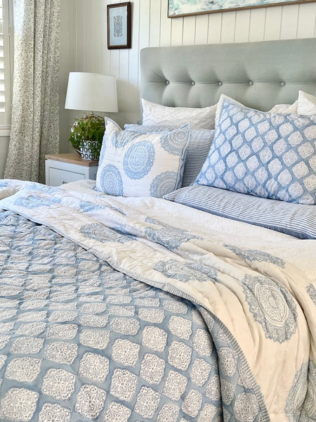 Neatly made bed with blue and white patterned bedding in a bedroom setting.