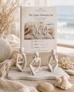 The Quiet Moments Set by Sunday Tide Design, featuring three small beige stone figurines in seated meditation poses on a wave-patterned base, styled with seashells, dried grass, and a neutral fabric backdrop.
