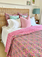 Bed with pink paisley comforter and colorful pillows in a bedroom setting.