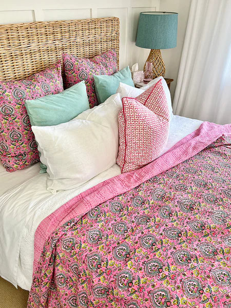 Bed with pink paisley comforter and colorful pillows in a bedroom setting.