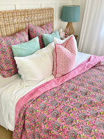 Bed with pink paisley comforter and colorful pillows in a bedroom setting.