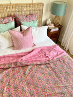 Bed with pink and white paisley bedding, wicker headboard, and nightstand with lamp.