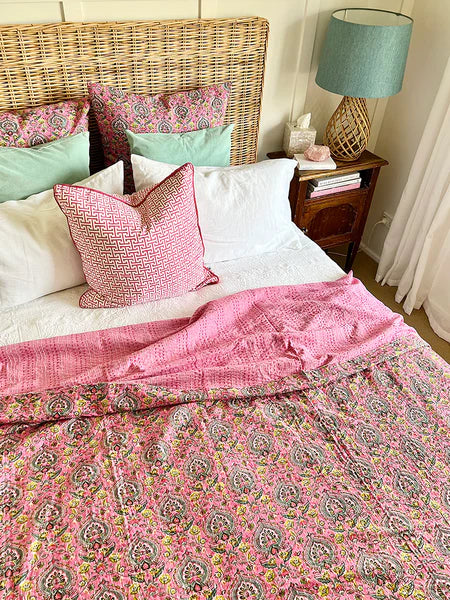 Bed with pink and white paisley bedding, wicker headboard, and nightstand with lamp.