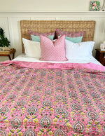 Bed with pink floral comforter and patterned pillows against a wooden headboard.