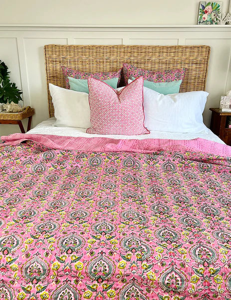 Bed with pink floral comforter and patterned pillows against a wooden headboard.