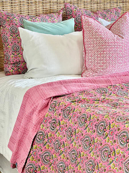 Bed with pink paisley comforter and pillows against a woven headboard