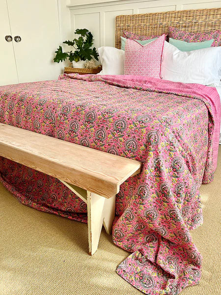 Bed with pink paisley comforter, white pillows, and a wooden bench.