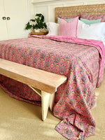 Bed with pink paisley comforter, white pillows, and a wooden bench.