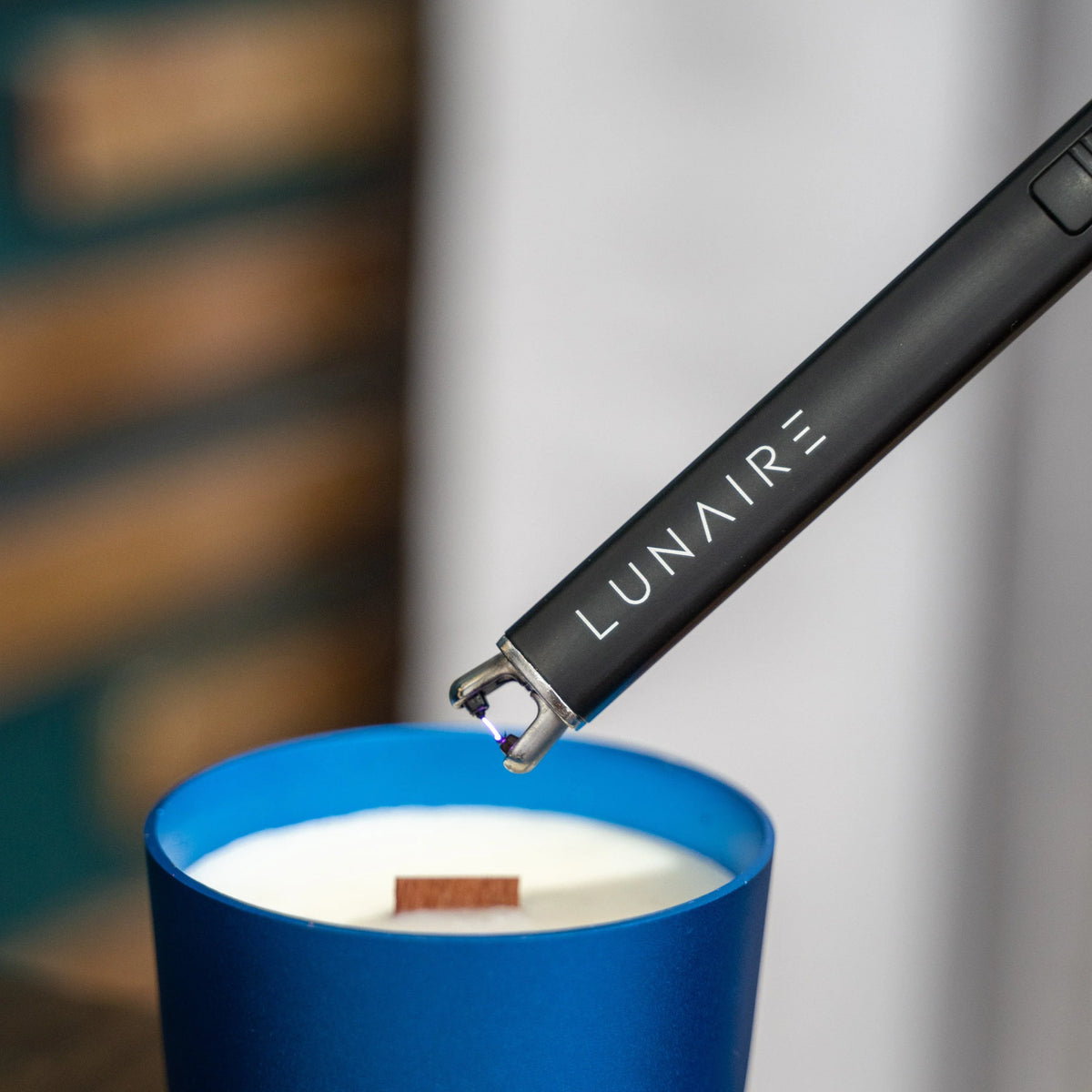 Lunaire lighter being used to light a candle in a blue holder.