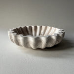 A scalloped ceramic bowl with a fluted rim, featuring a marbled pattern in off-white, beige, and gray, set against a neutral gray background.