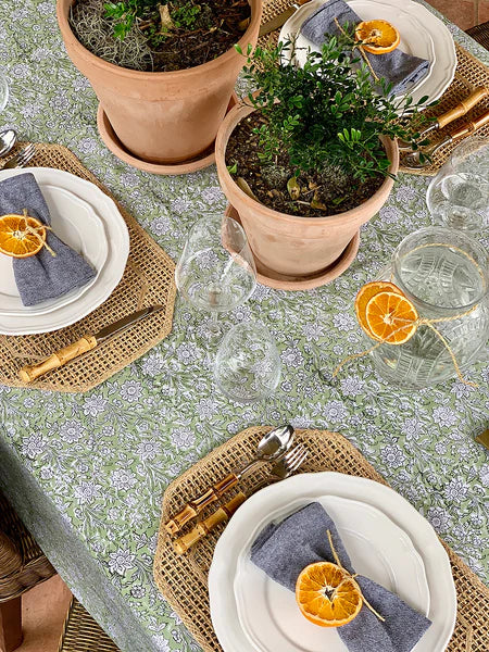 Table setting with plates, glasses, and potted plants on a floral tablecloth.