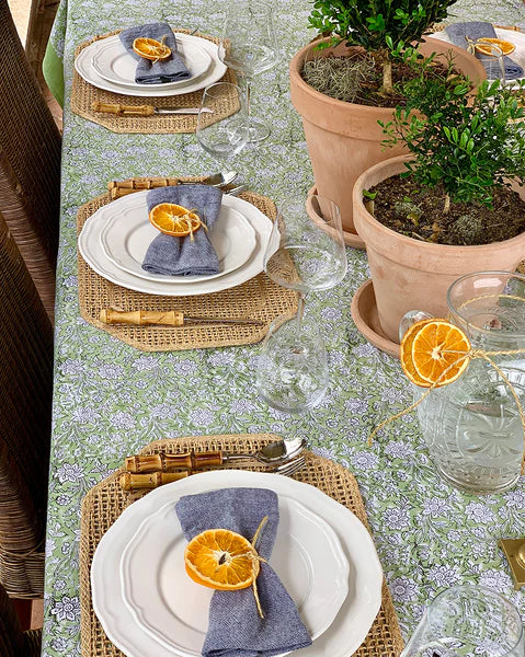 Dining table setting with floral tablecloth, plates, napkins, and decorative oranges.