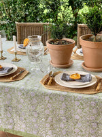 Outdoor table setting with floral tablecloth, plates, glasses, and potted plants.