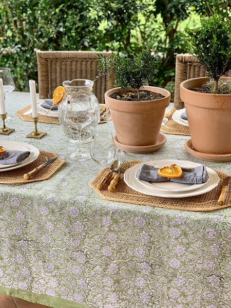 Outdoor table setting with floral tablecloth, plates, glasses, and potted plants.