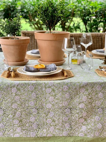 Outdoor table setting with floral tablecloth, potted plants, and glasses.