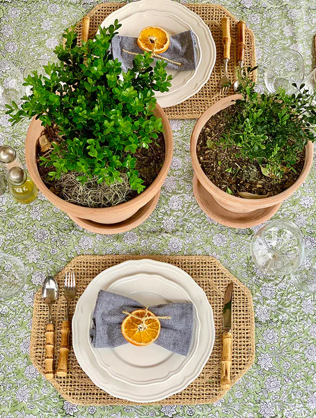 Decorative table setting with potted plants, plates, and cutlery on a patterned tablecloth.