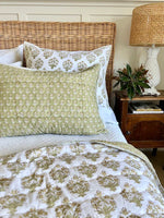 Bed with floral bedding and pillows, wicker headboard, and lamp on nightstand.