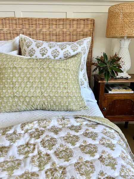Bed with floral bedding and pillows, wicker headboard, and lamp on nightstand.