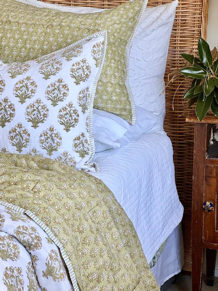 Bed with green and white patterned bedding next to a wooden side table with a plant.