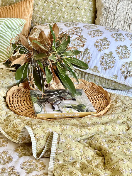 Decorative arrangement with greenery on a wicker tray over a patterned blanket